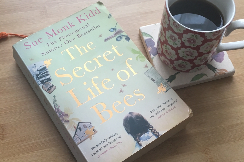 The book cover for "The Secret Life of Bees" by Sue Monk Kidd with a cup of coffee next to it